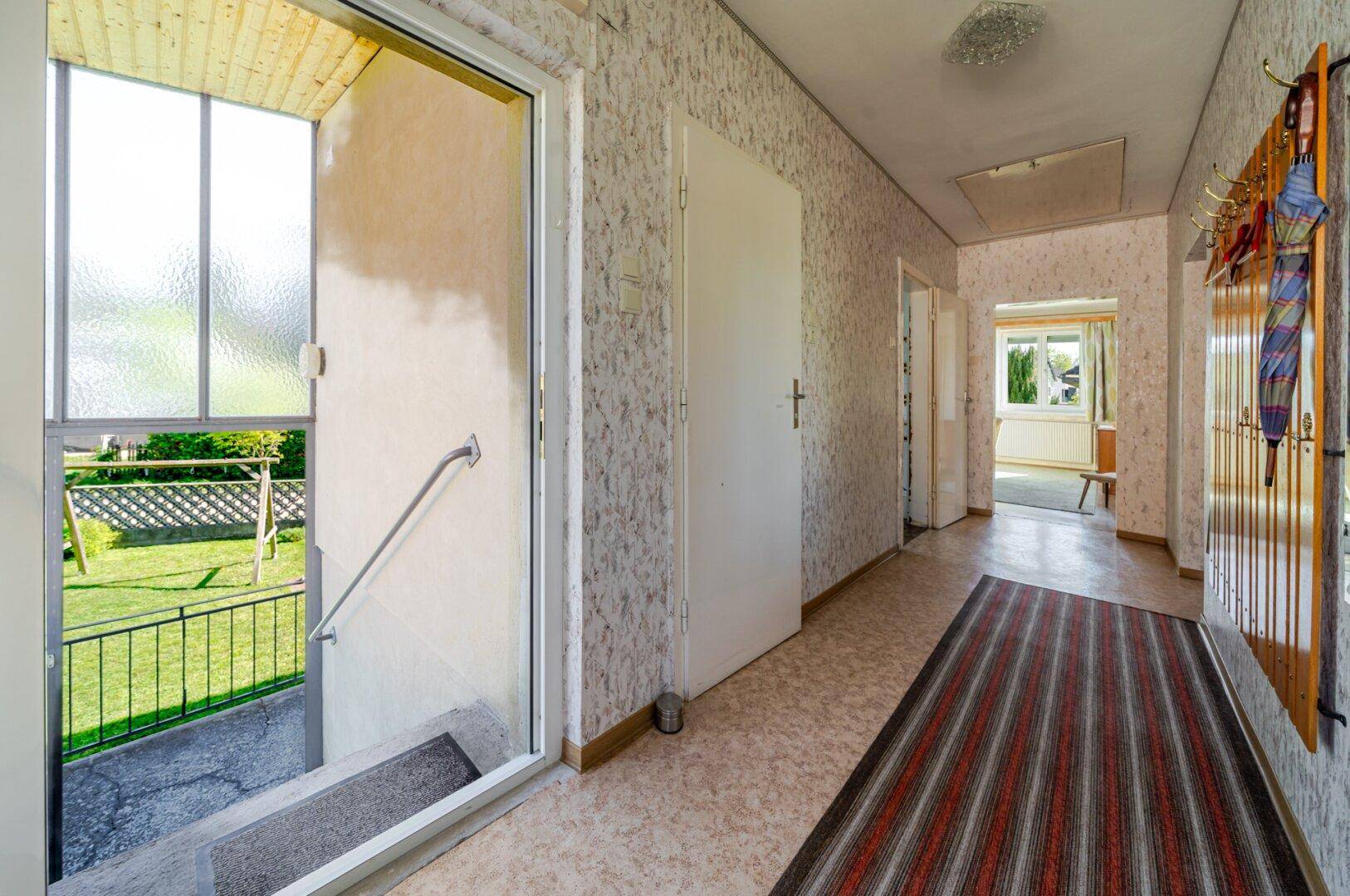 Heller Flur mit gemusterter Tapete und Zugang zum Gartenbereich über eine Treppe.