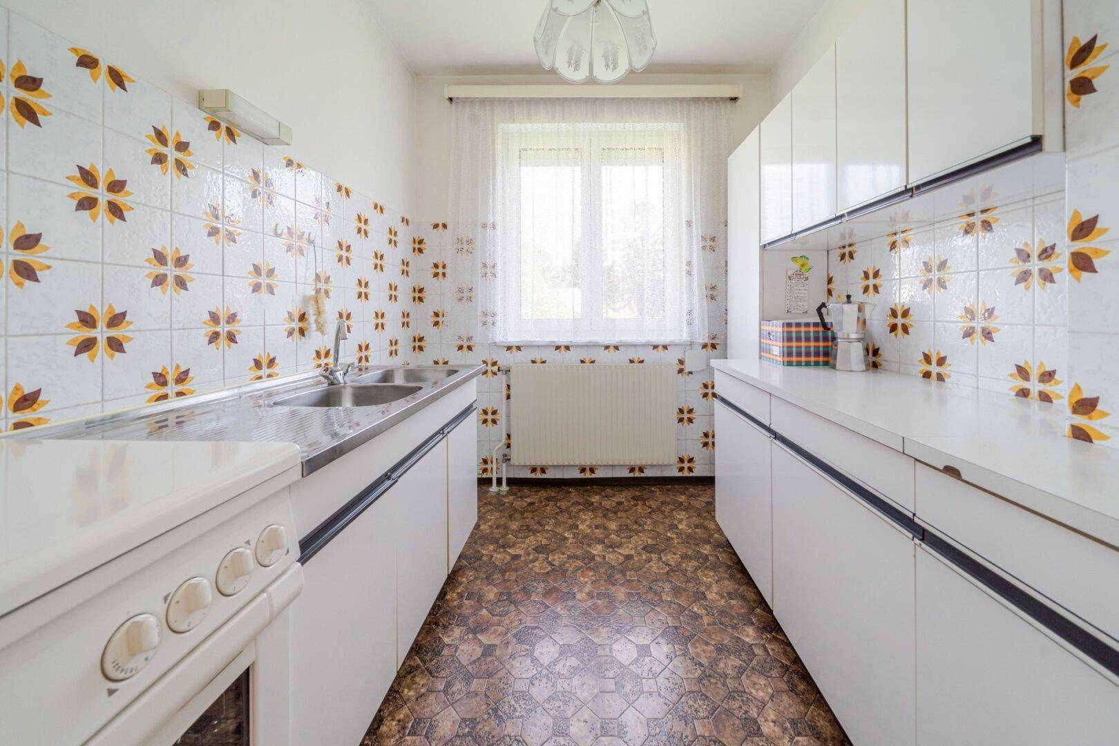 Küche im Retro-Stil mit weißen Schränken, gemusterten Fliesen und Fenster über der Spüle.