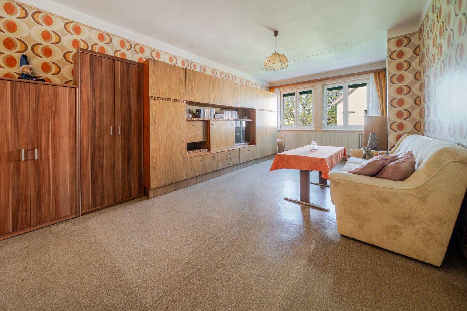 Wohnzimmer im Vintage-Stil mit gemusterter Tapete, Holzmöbeln und Blick ins Grüne.