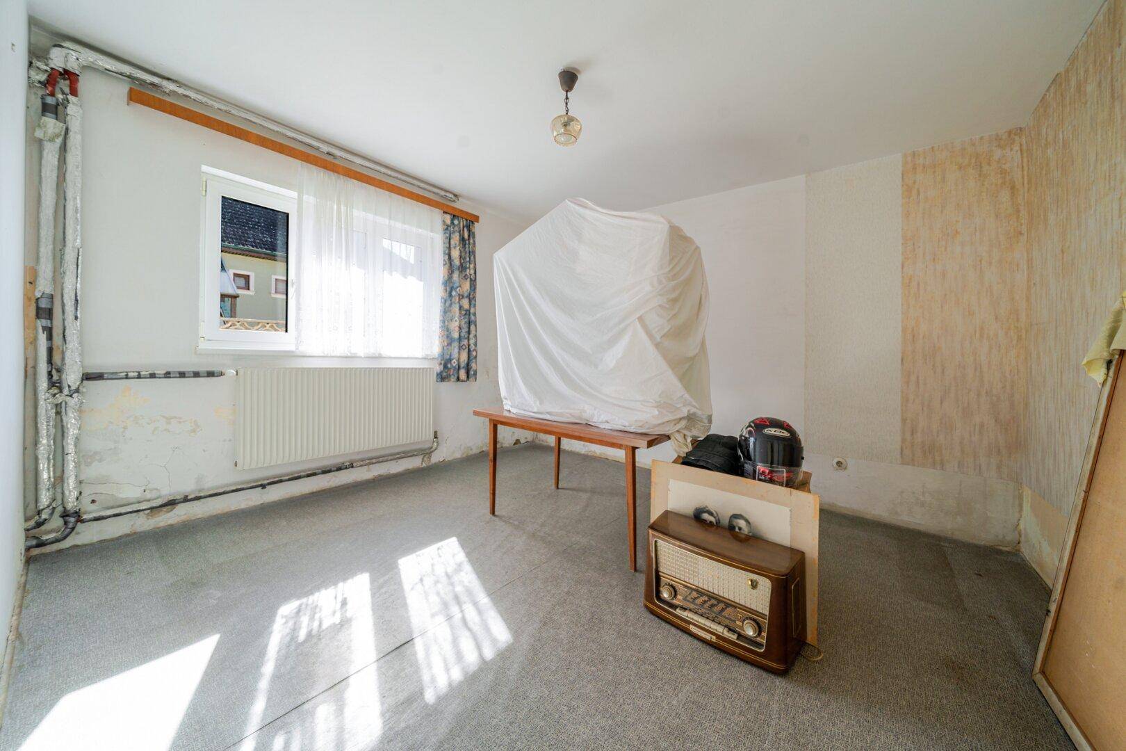 Raum in ursprünglichem Zustand mit Teppichboden, Fenster und einem Vintage-Radio.