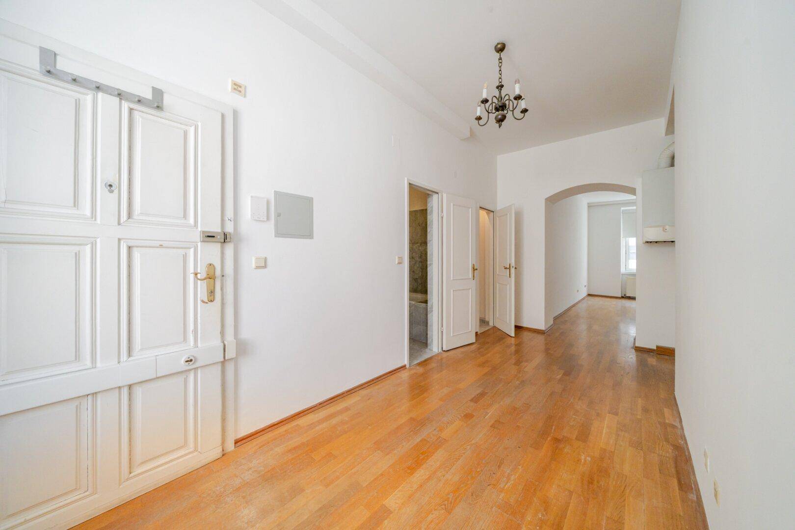 Heller Flur mit Holzboden, weißer Eingangstür und Durchgang zu weiteren Räumen der Wohnung.