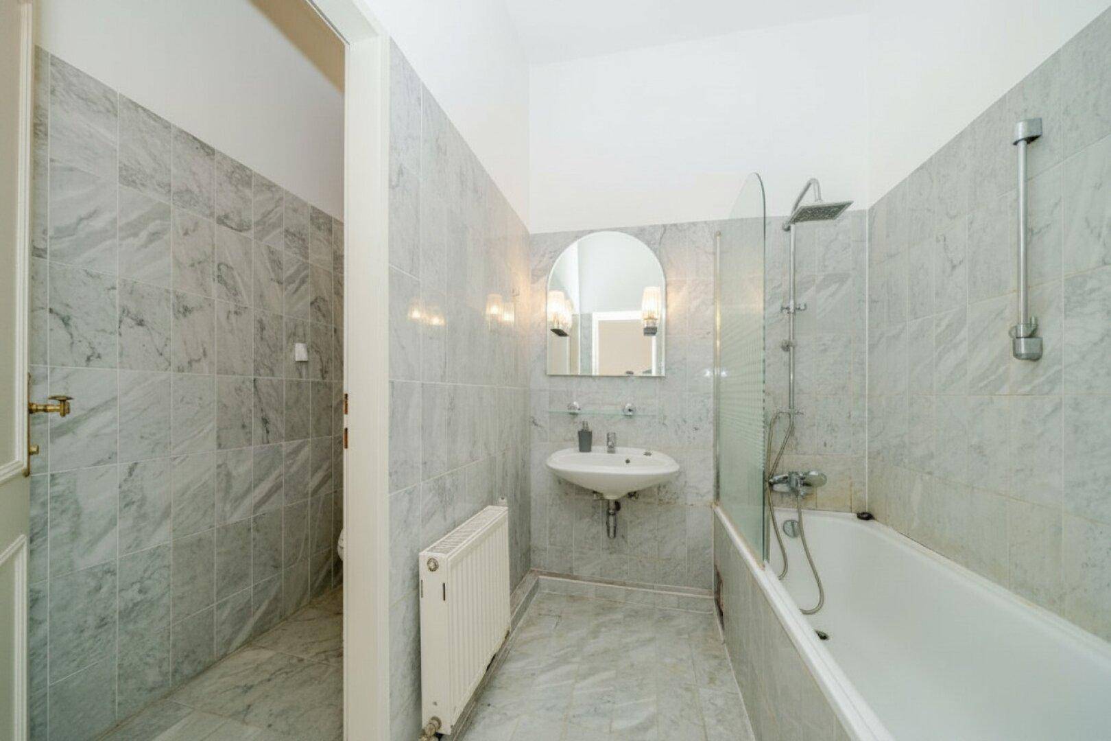 Modernes Badezimmer mit grauen Marmorfliesen, Badewanne mit Duschvorrichtung und Waschbecken.