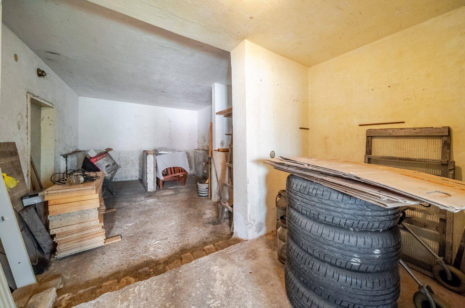 Unfertiger Kellerraum mit Betonboden und Lagerfläche für diverse Gegenstände, ideal als Abstellraum.