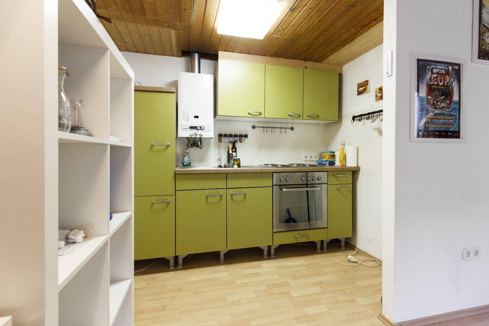 Kleine, funktionale Kochnische mit grünen Schränken, Gasherd und Holzbalkendecke, praktisch eingerichtet.