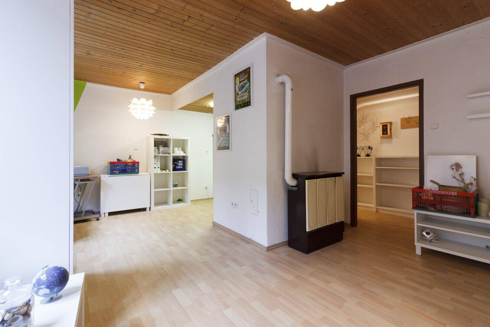 Geräumiger Wohnbereich mit Holzbalkendecke, Laminatboden und einem gemütlichen Kaminofen.