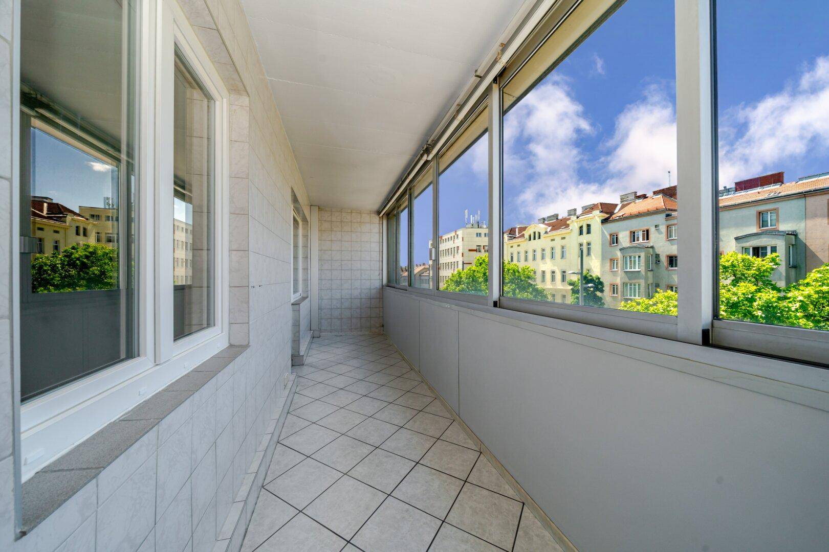 Lange, geflieste Loggia mit großen Fenstern bietet einen Blick auf die umliegenden Stadtgebäude und Bäume.