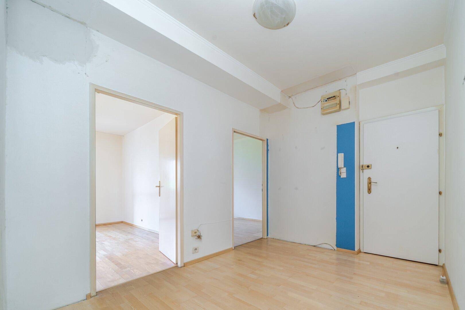 Heller Flur mit Parkettboden und weißen Wänden, der zu mehreren Zimmern führt, akzentuiert durch eine blaue Wand.