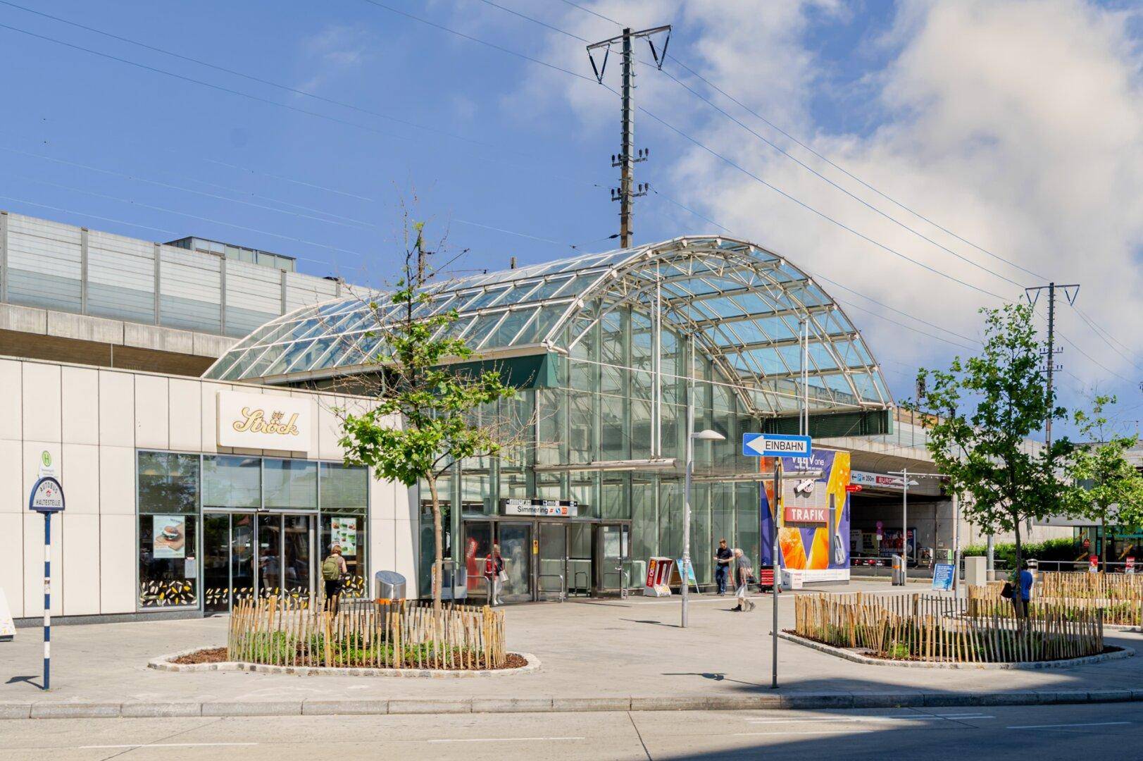 Modernes Gebäude mit großer Glaskuppel, wahrscheinlich ein Bahnhof oder Verkehrsknotenpunkt, umgeben von Bäumen.