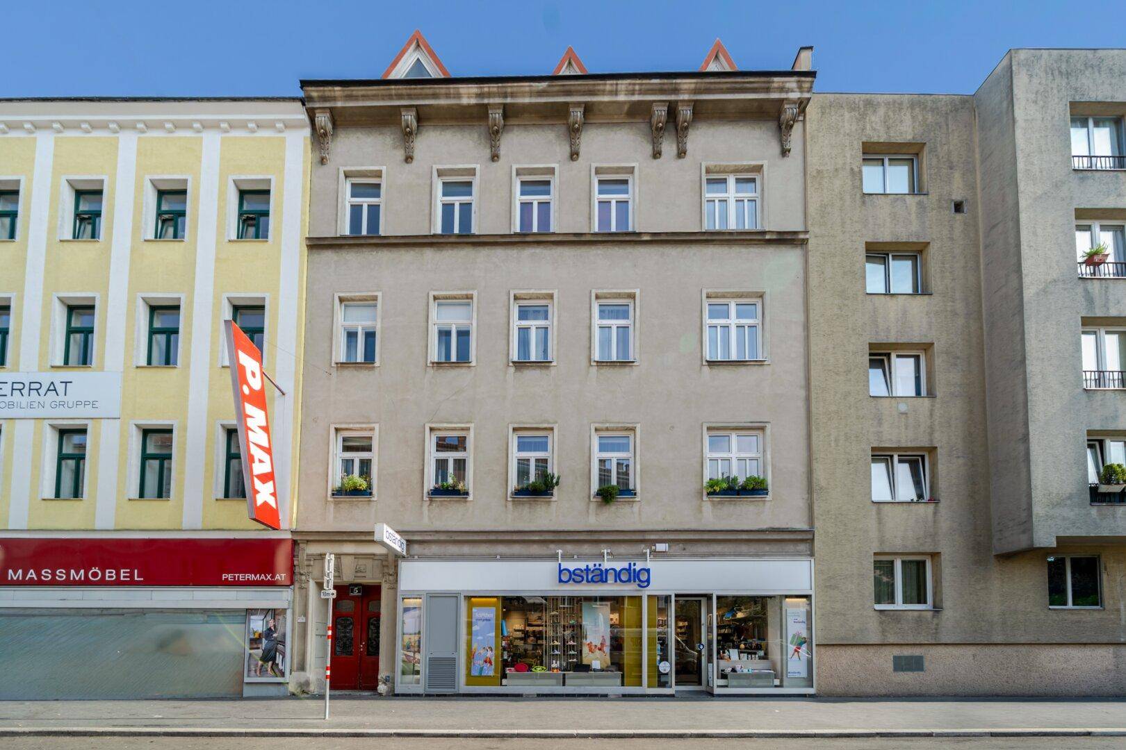 Fassade eines Mehrfamilienhauses mit Geschäften im Erdgeschoss und vielen Fenstern.