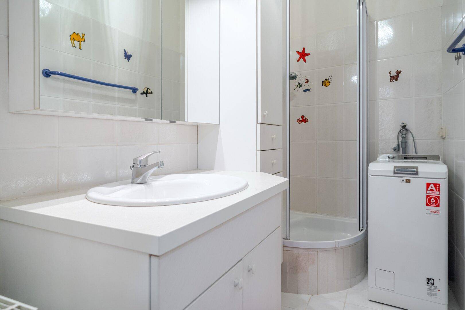 Helles Badezimmer mit Duschkabine, Waschbecken und praktischer Waschmaschine.