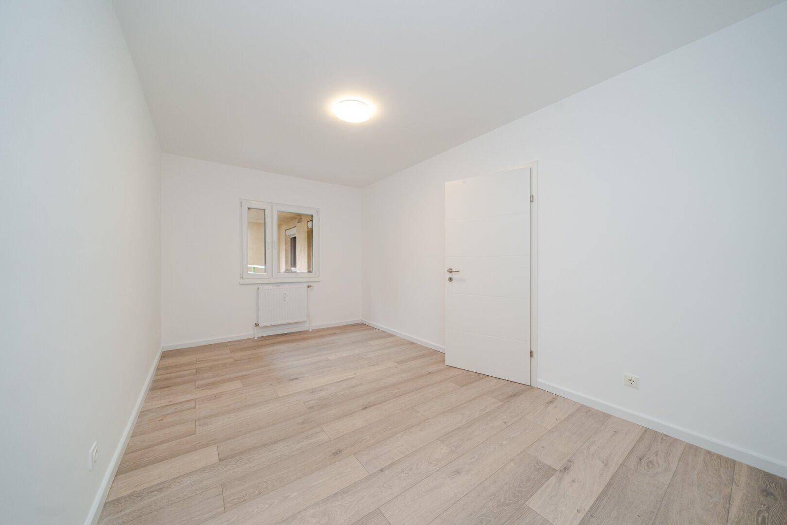 Helles Schlafzimmer mit Laminatboden und weißer Tür, bereit zur individuellen Gestaltung.