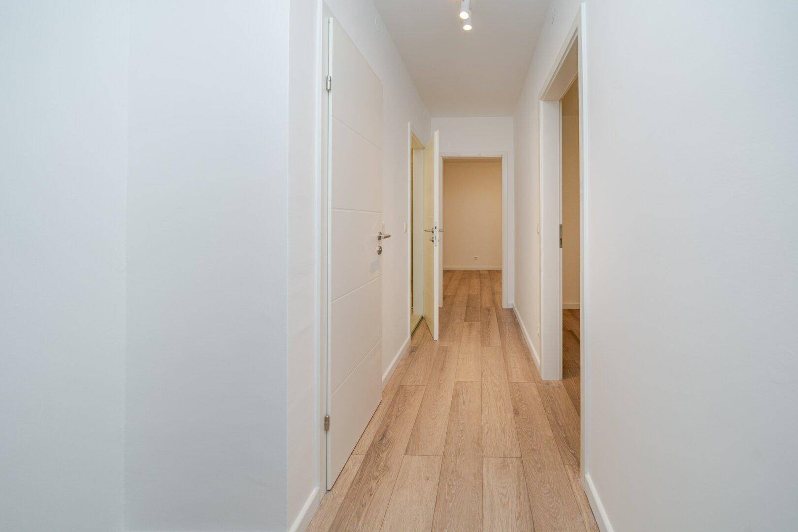 Heller Flur mit Laminatboden und weißen Türen, der zu den verschiedenen Räumen führt.