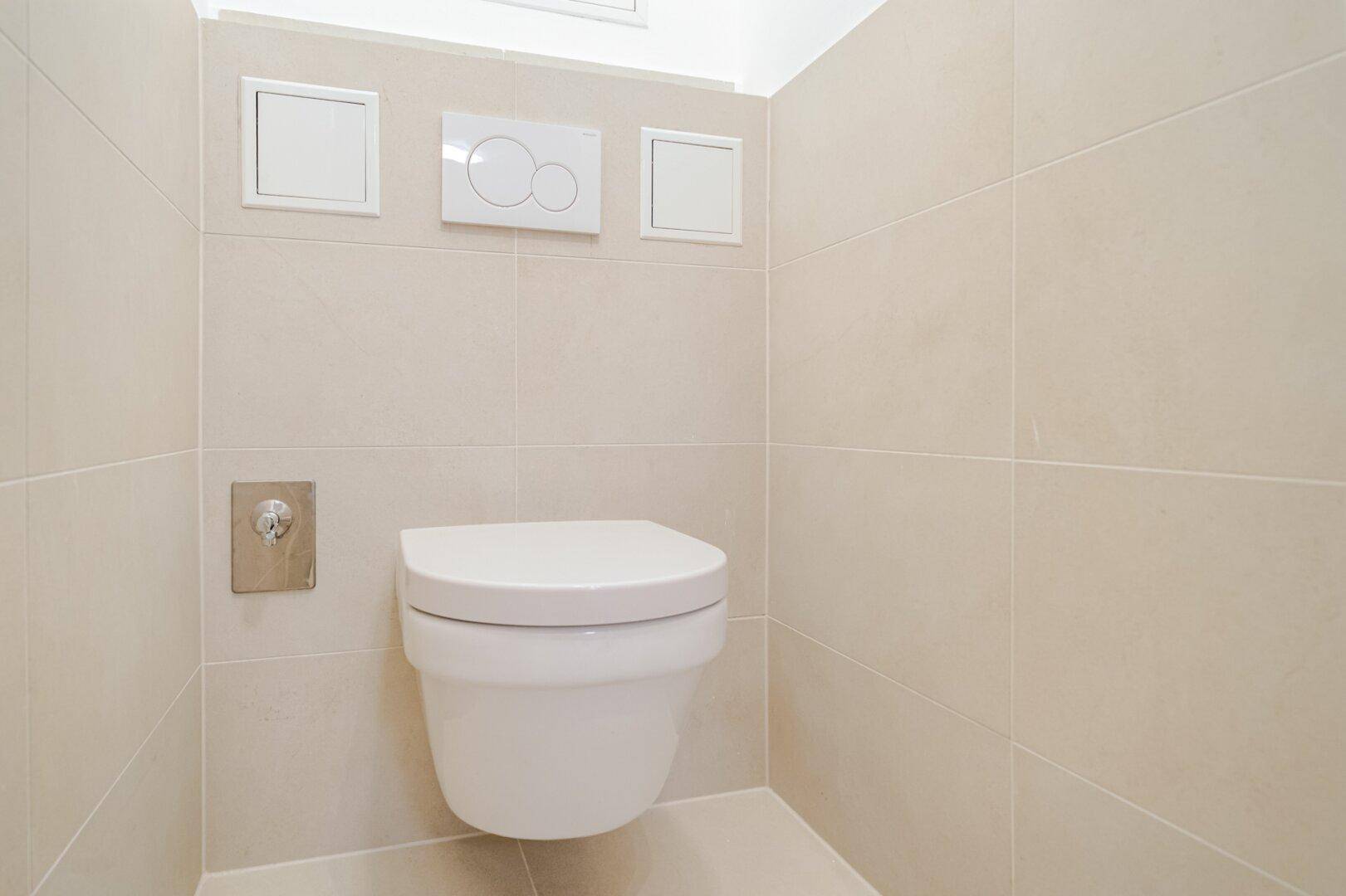 Separates WC mit wandhängender Toilette und hellen, modernen Fliesen.
