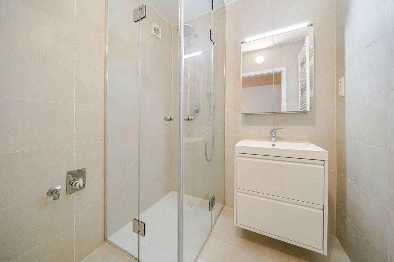 Modernes Badezimmer mit begehbarer Dusche, Waschbecken und hellen Fliesen.