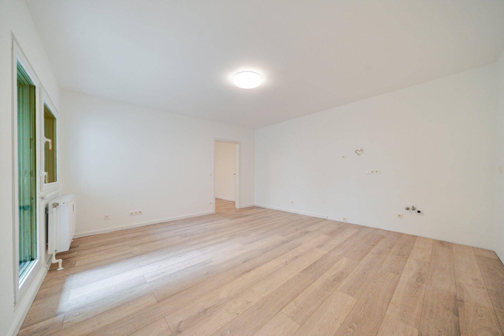 Geräumiges, helles Zimmer mit Laminatboden und weiß gestrichenen Wänden.