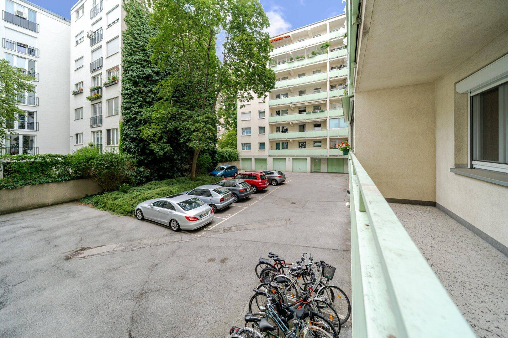 Blick von einem Balkon auf den Innenhof mit Parkplätzen, Fahrrädern und umliegenden Wohngebäuden.