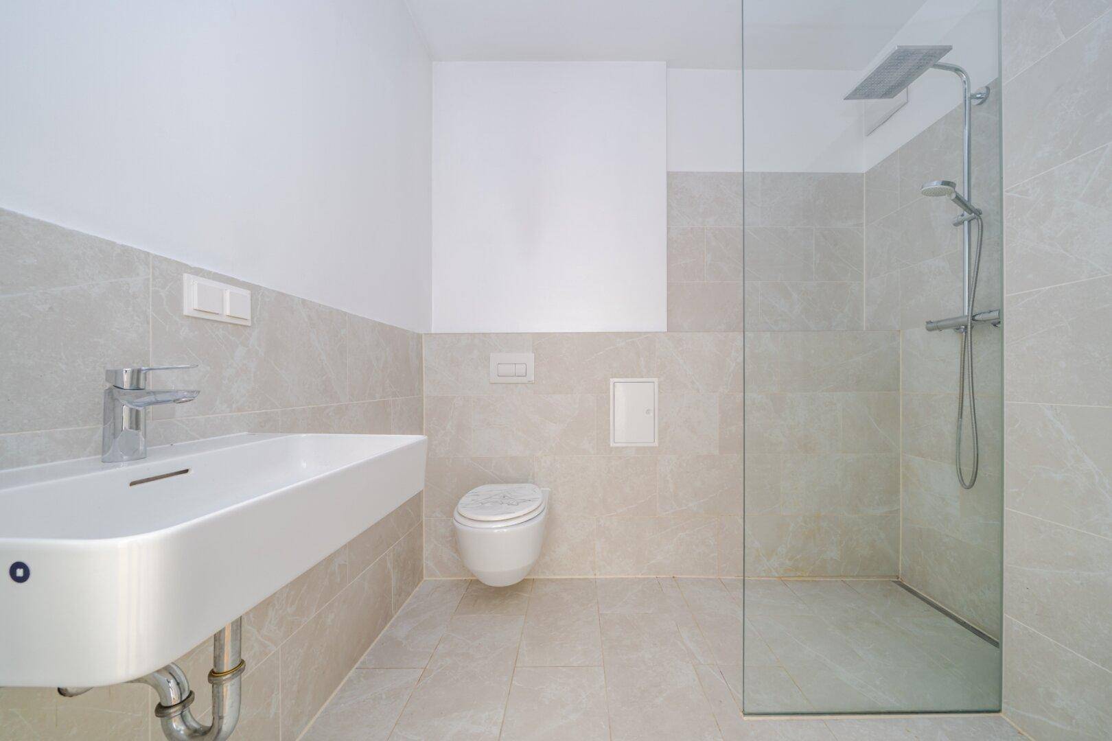 Modernes Badezimmer mit hellgrauen Fliesen, wandhängendem WC und geräumiger begehbarer Dusche.