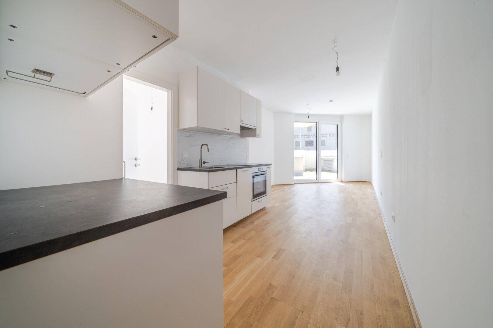 Heller offener Wohnbereich mit neuer Einbauküche, Holzboden und Zugang zur Terrasse.