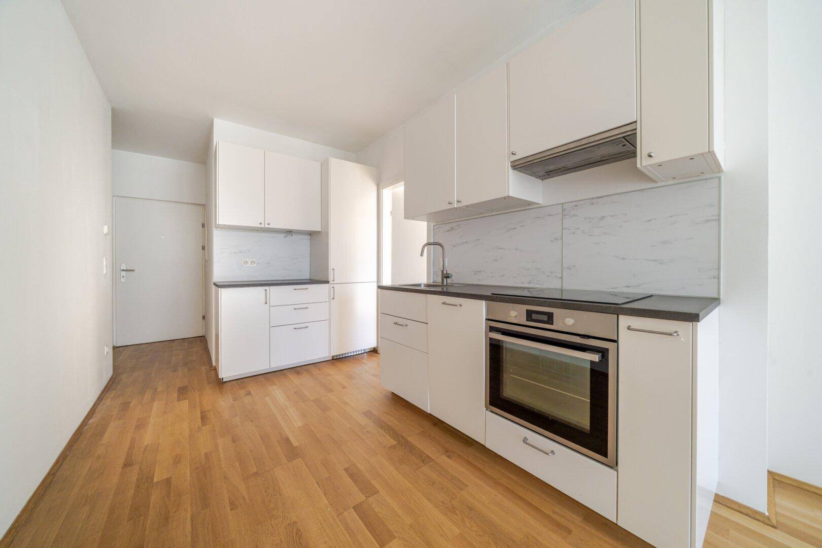 Moderne Einbauküche mit weißen Schränken, dunkler Arbeitsplatte und integrierten Geräten.