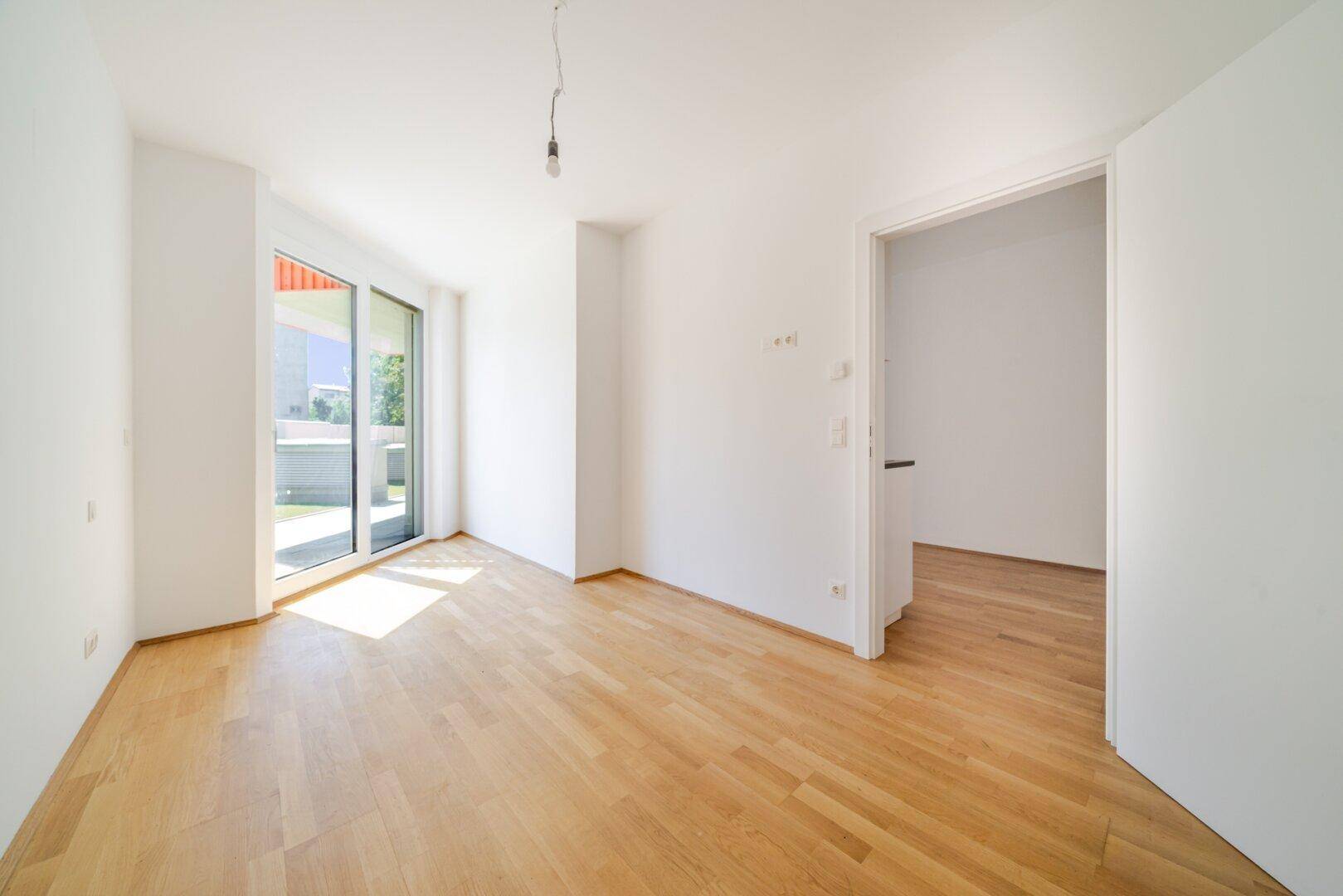 Heller Wohnraum mit Holzboden, großen Fenstern und viel Tageslicht, bereit zur individuellen Gestaltung.