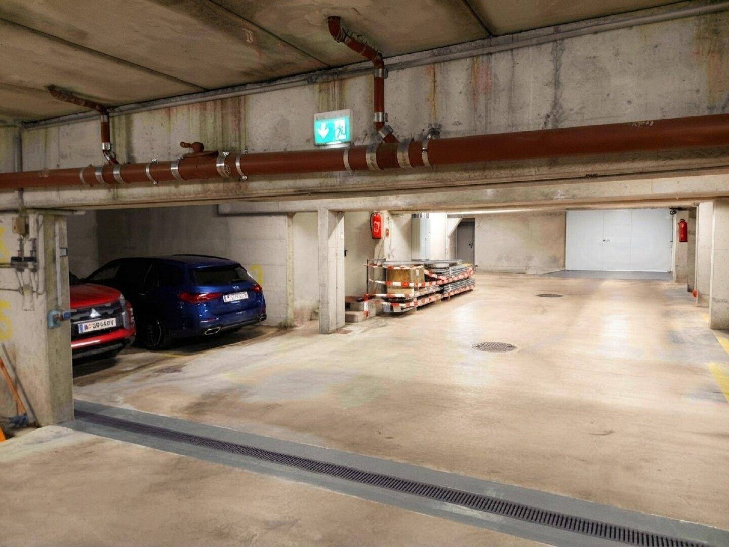 Tiefgarage mit geparkten Autos, sichtbaren Rohren an der Decke und Brandschutzeinrichtungen.