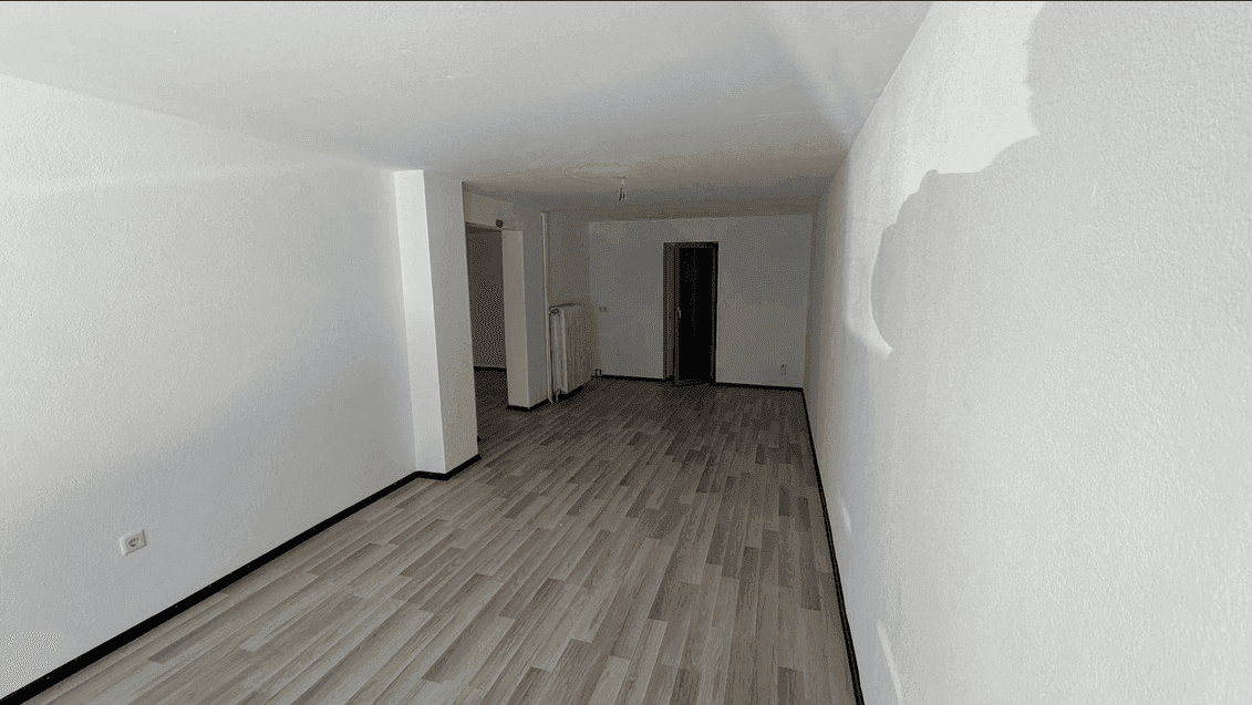 Langer, leerer Raum mit weißen Wänden, hellem Laminatboden und einem Heizkörper an der Wand.