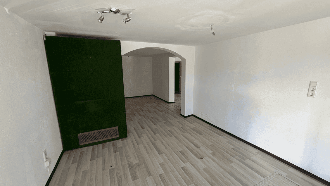 Leerer Raum mit hellem Laminatboden, einer grünen Akzentwand und einem Bogen im Hintergrund.