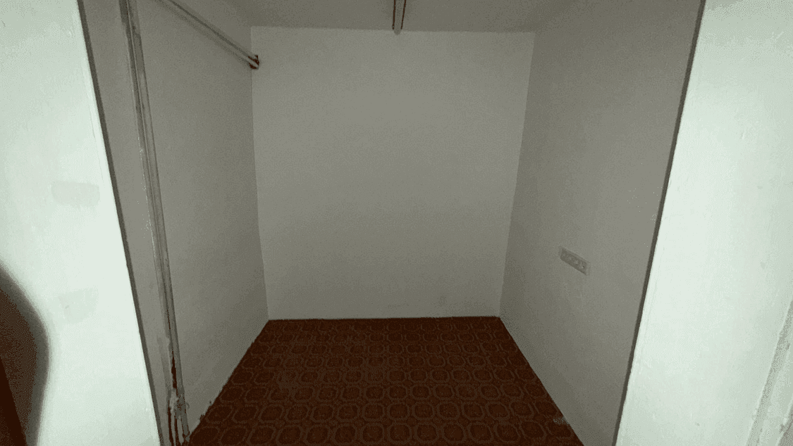 Kleiner, leerer Abstellraum mit dunklem, gemustertem Boden und einer Kleiderstange an der Wand.