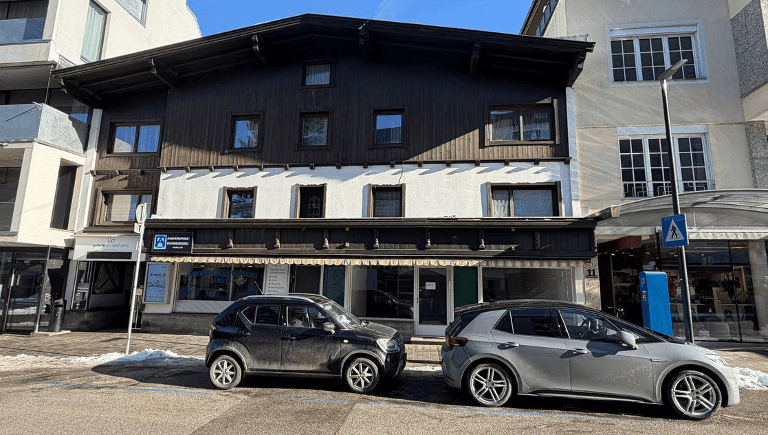 Traditionelle Gebäudefassade mit dunklem Holz und weißem Putz, davor parken Autos auf der Straße.