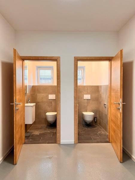 Flur mit zwei offenen Türen, die zu separaten, modern gefliesten Toilettenräumen führen.