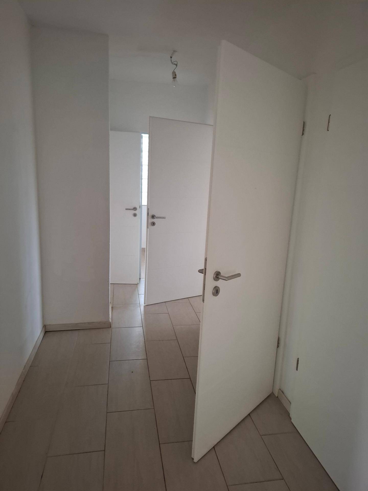 Heller Flur mit Fliesenboden und weißen Türen, die zu verschiedenen Räumen führen.