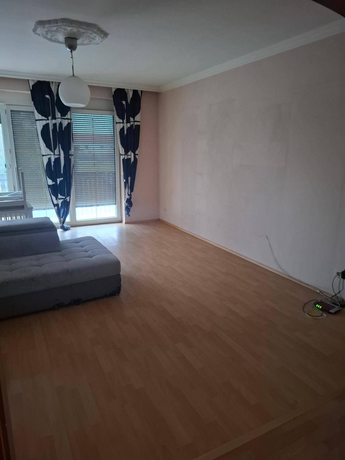 Geräumiges Wohnzimmer mit Laminatboden, Stuckdecke und Zugang zu einem Balkon.