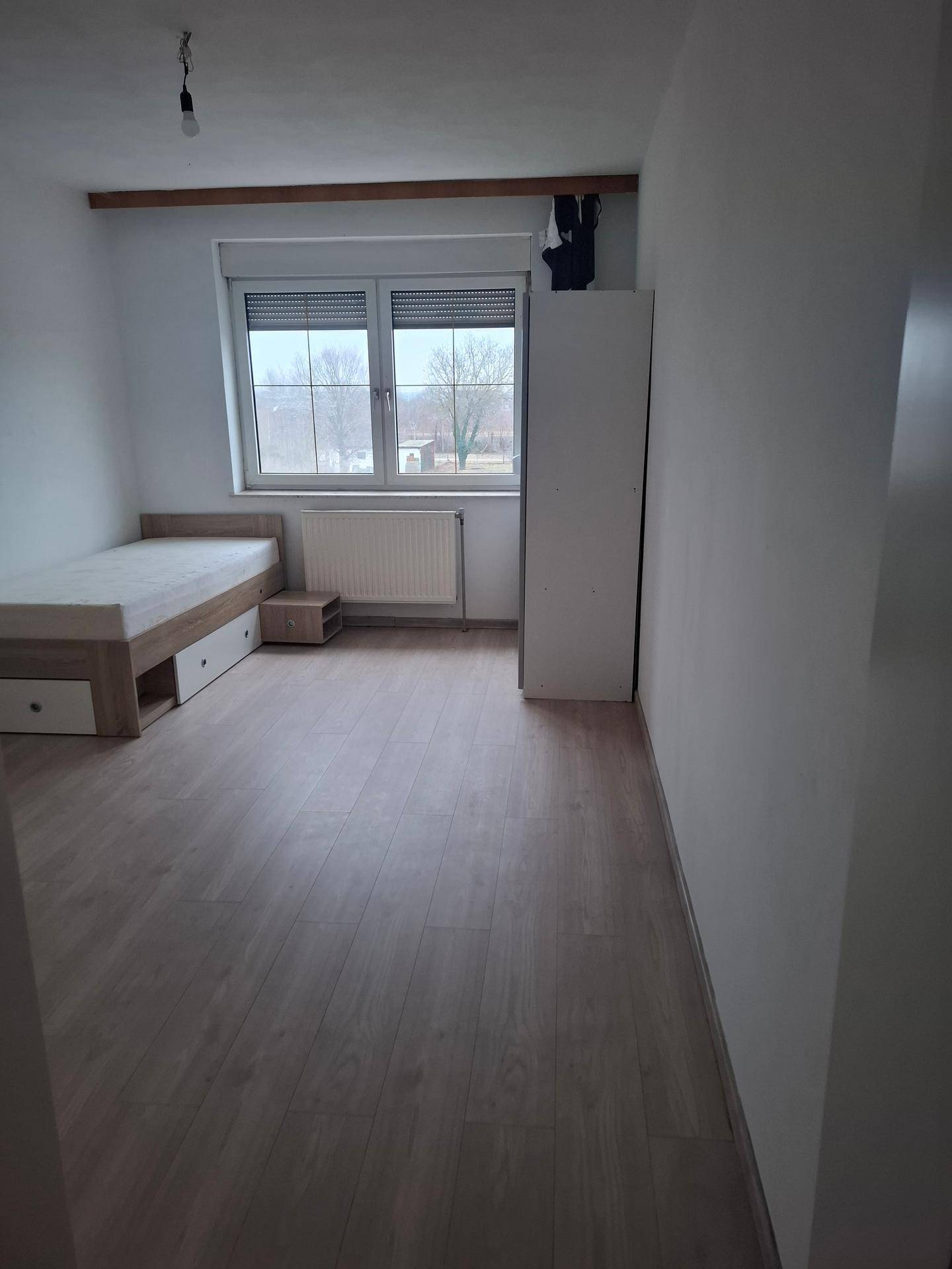 Helles Schlafzimmer mit Laminatboden, Einzelbett und Fenster mit Blick ins Grüne.