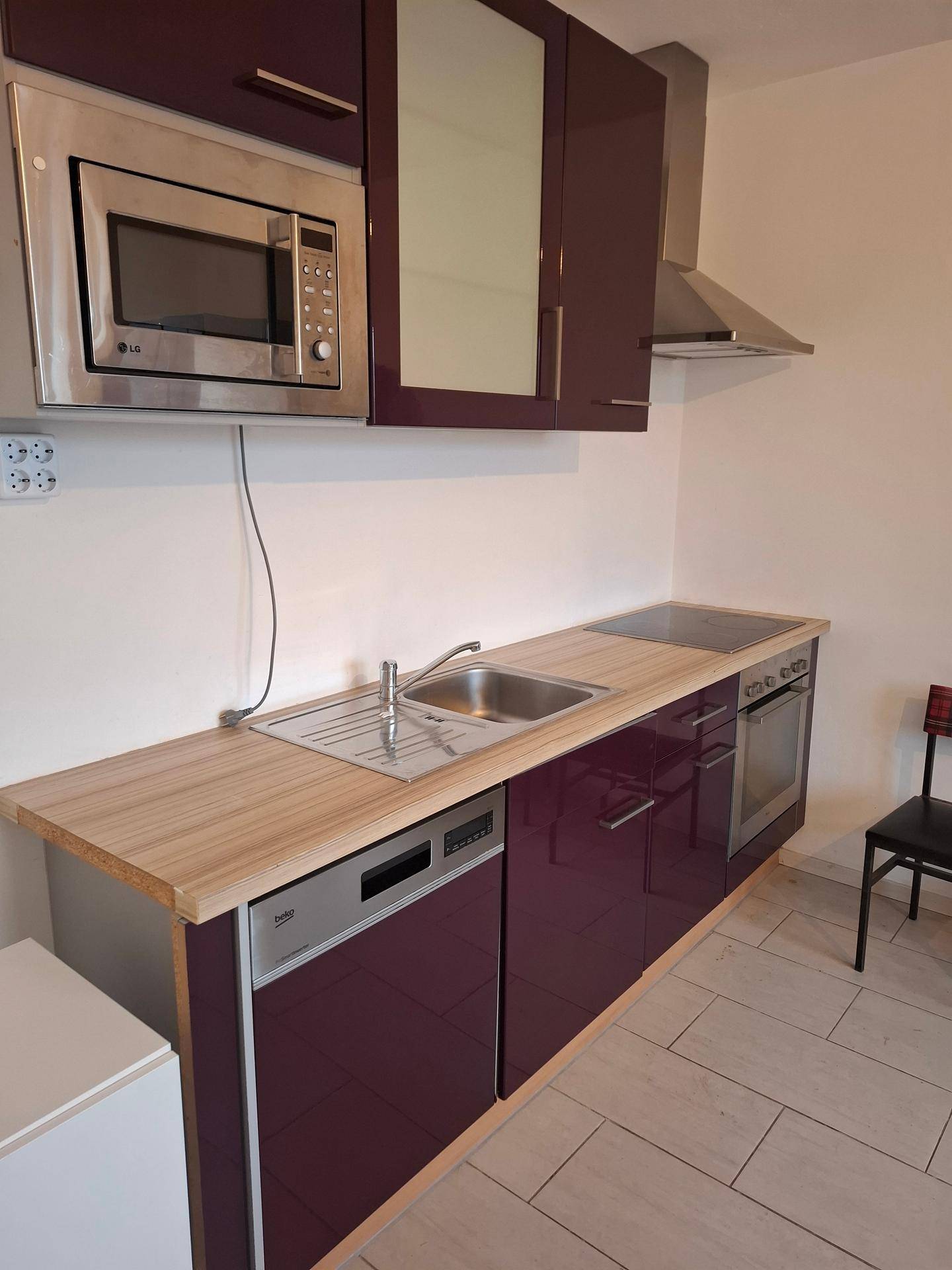 Moderne Küchenzeile mit lila Hochglanzfronten, Spüle und integrierten Geräten.