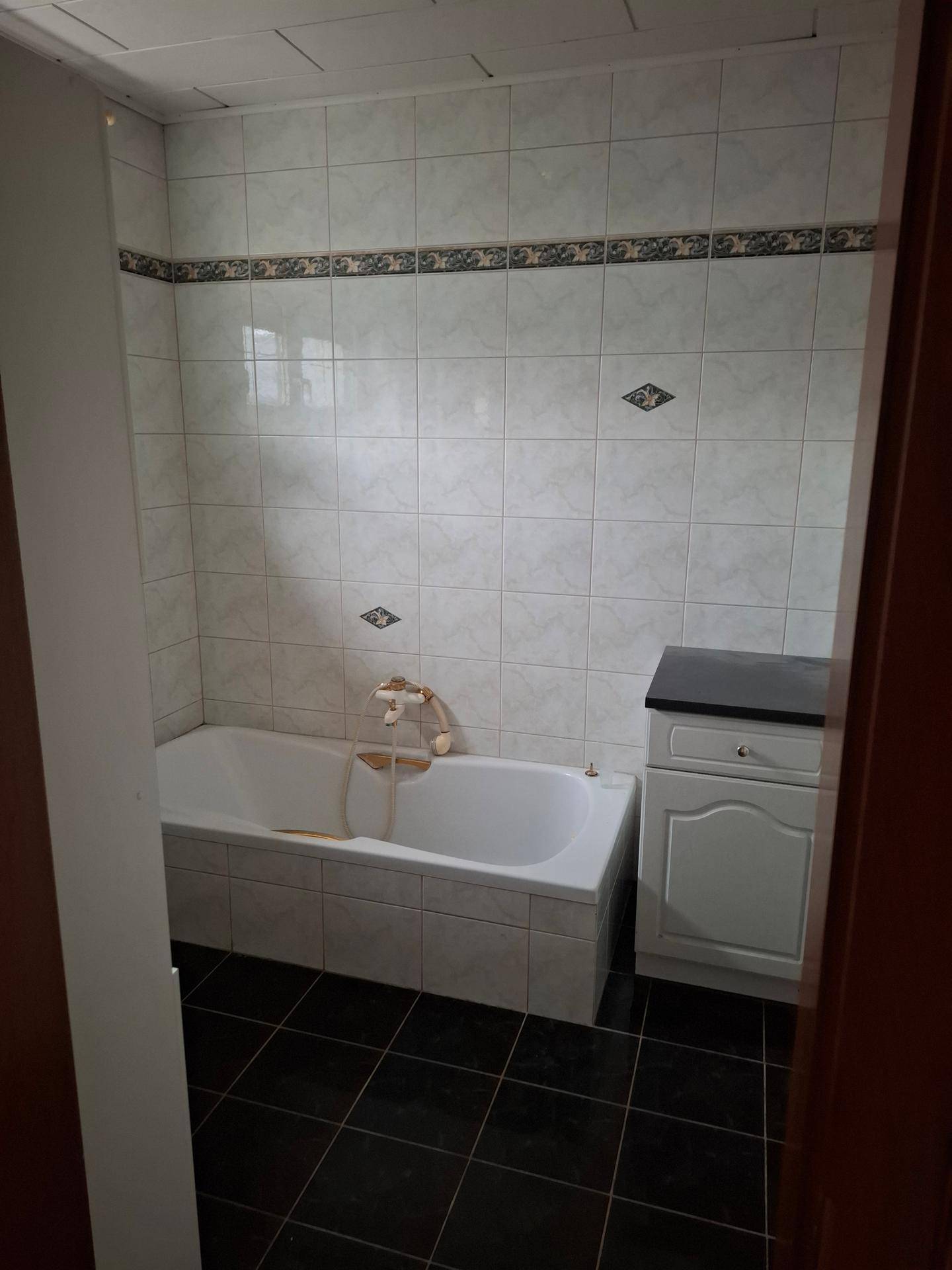 Gefliestes Badezimmer mit Badewanne, dunklem Boden und einem kleinen Waschtisch.