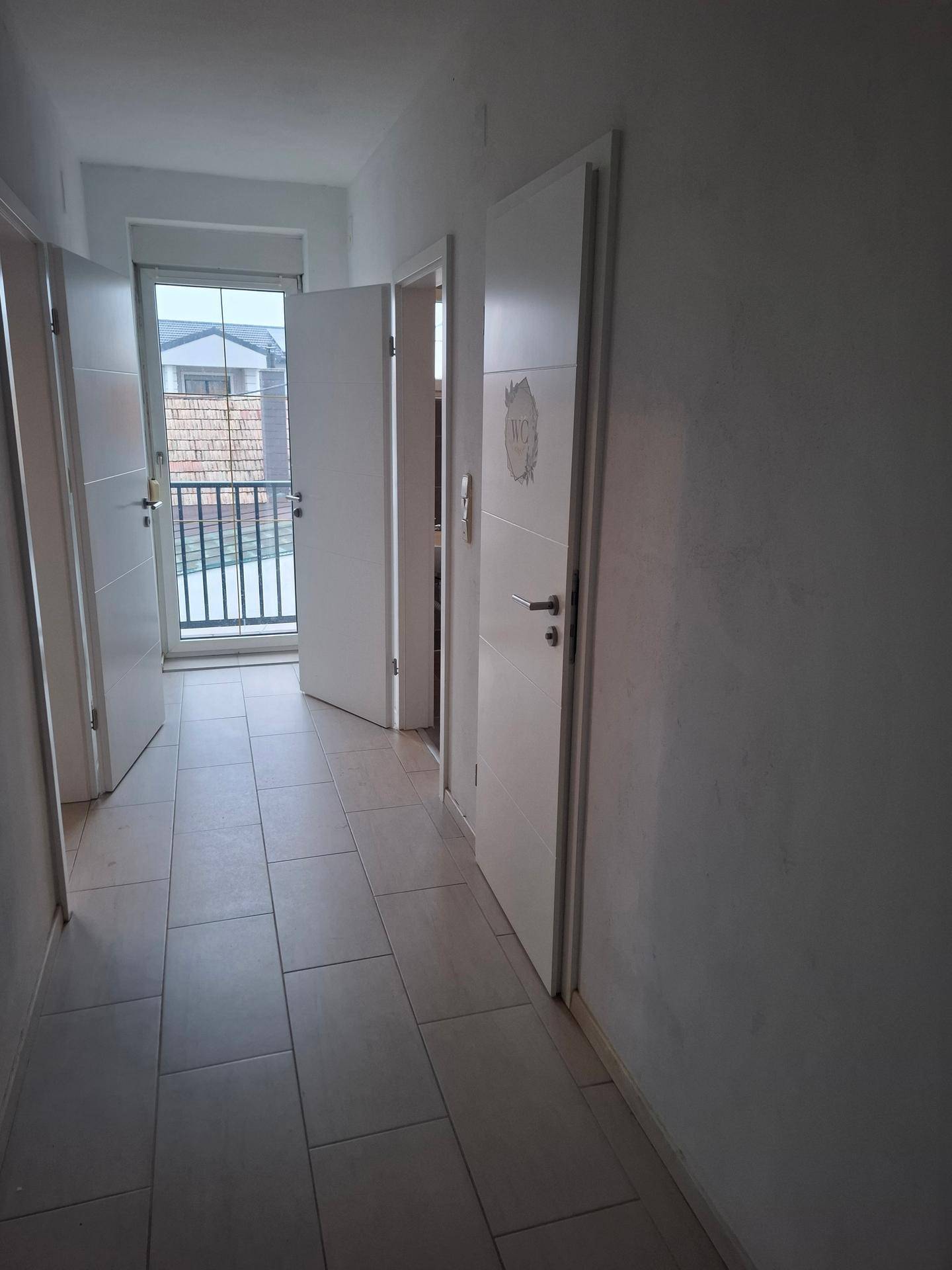 Heller Flur mit Fliesenboden, weißen Türen und Zugang zu einem Balkon.