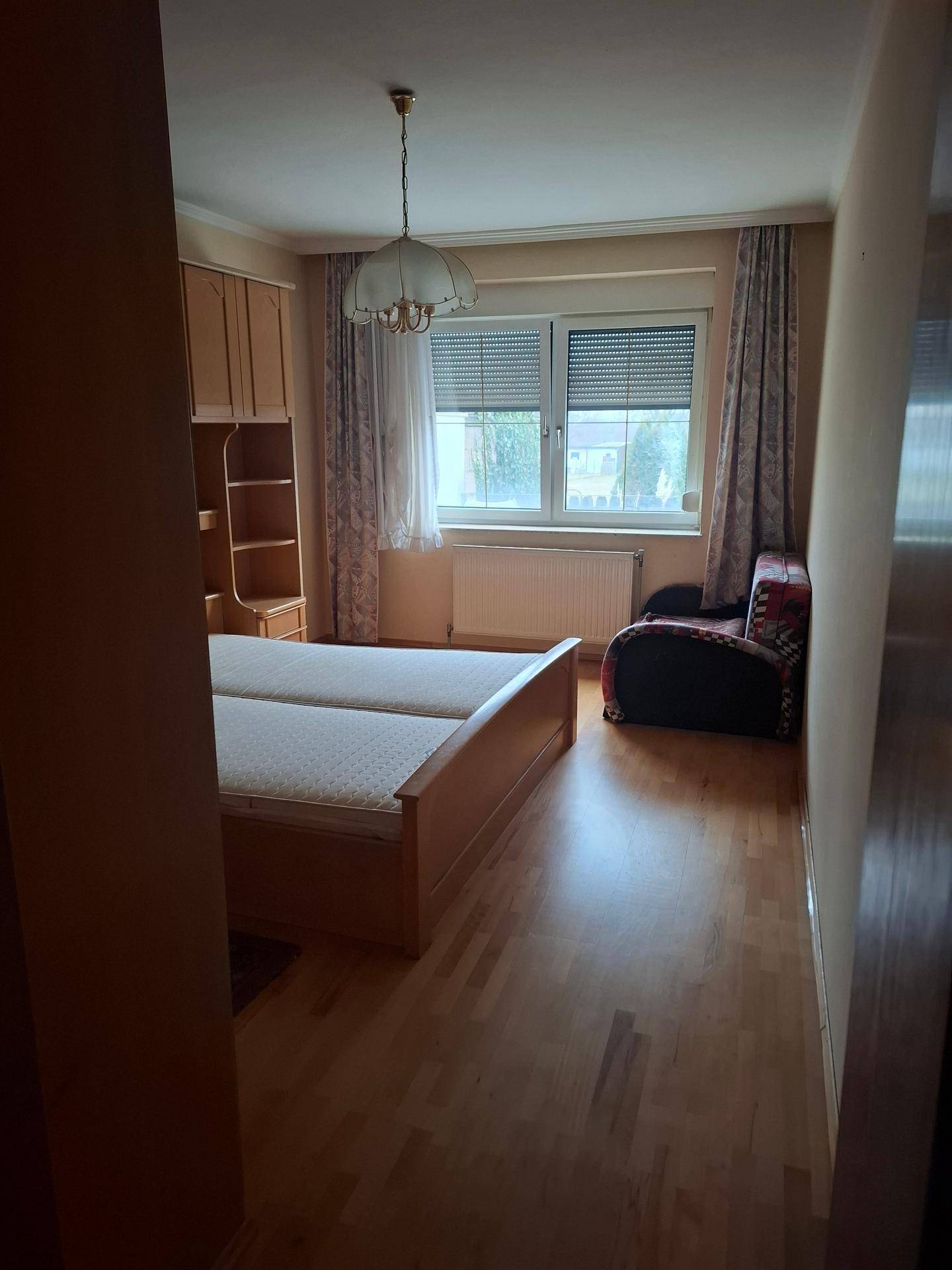 Gemütliches Schlafzimmer mit Holzmöbeln, zwei Einzelbetten und Fenster mit Vorhängen.