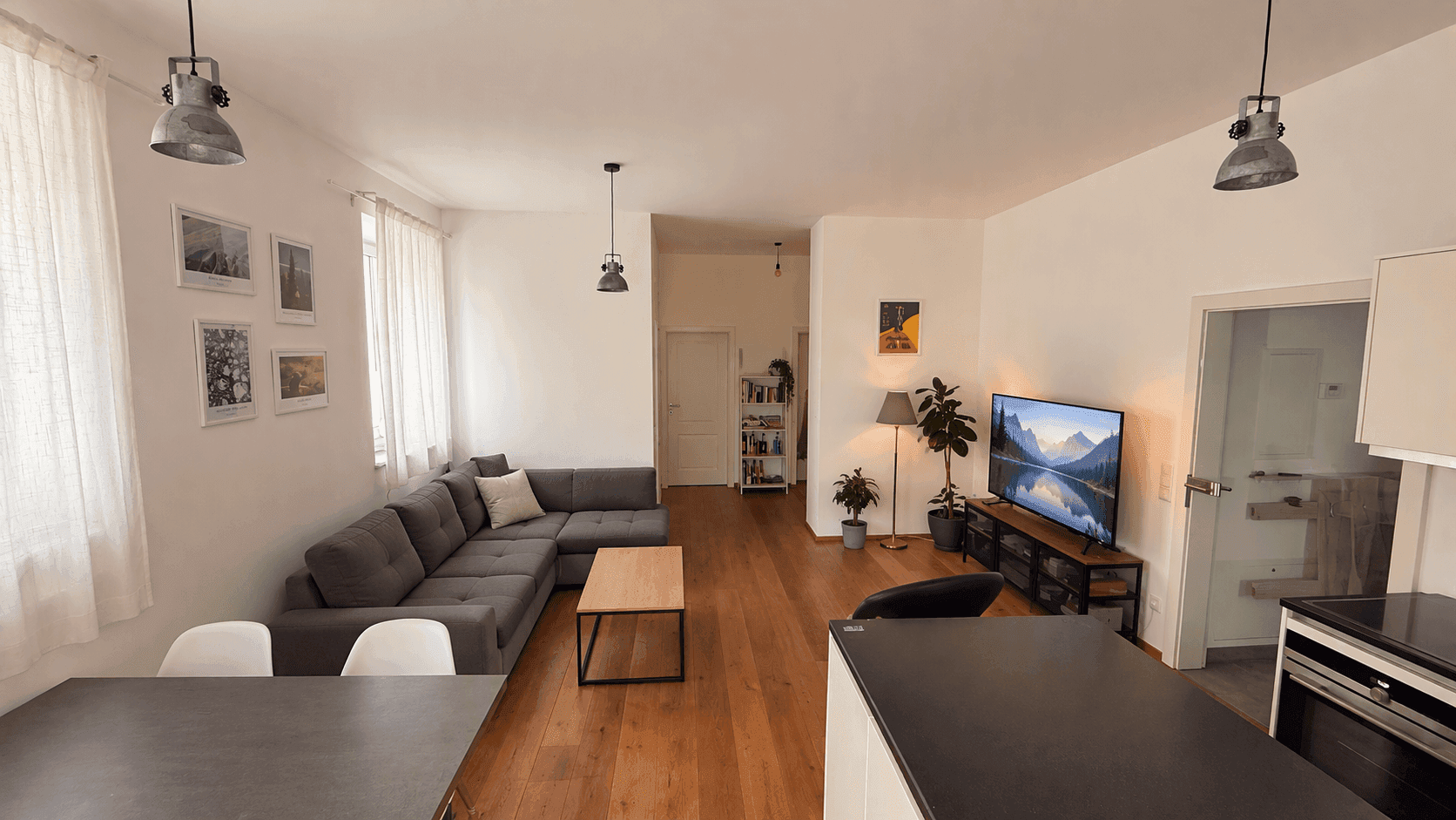 Weitläufiger offener Wohn-Essbereich mit Küche, Sofa und Holzboden.