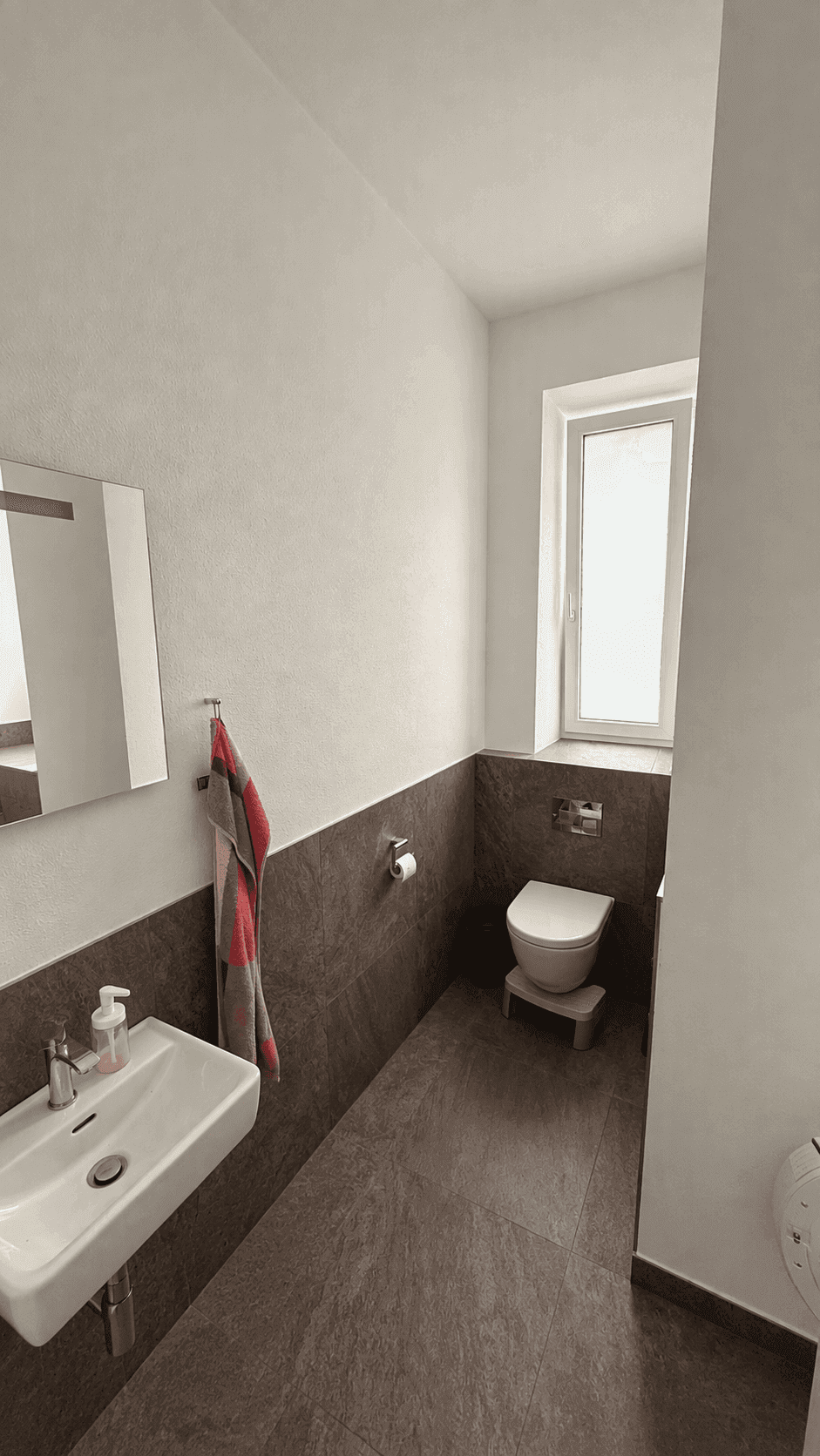 Modernes Gäste-WC mit Wand-WC, kleinem Waschbecken und Fenster.