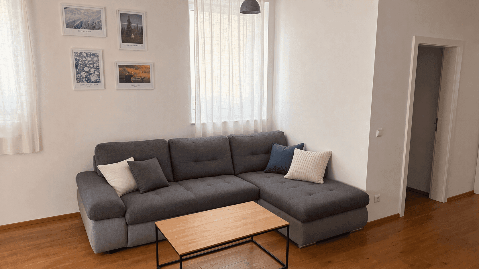 Helles Wohnzimmer mit grauem Ecksofa, Couchtisch und Holzboden.