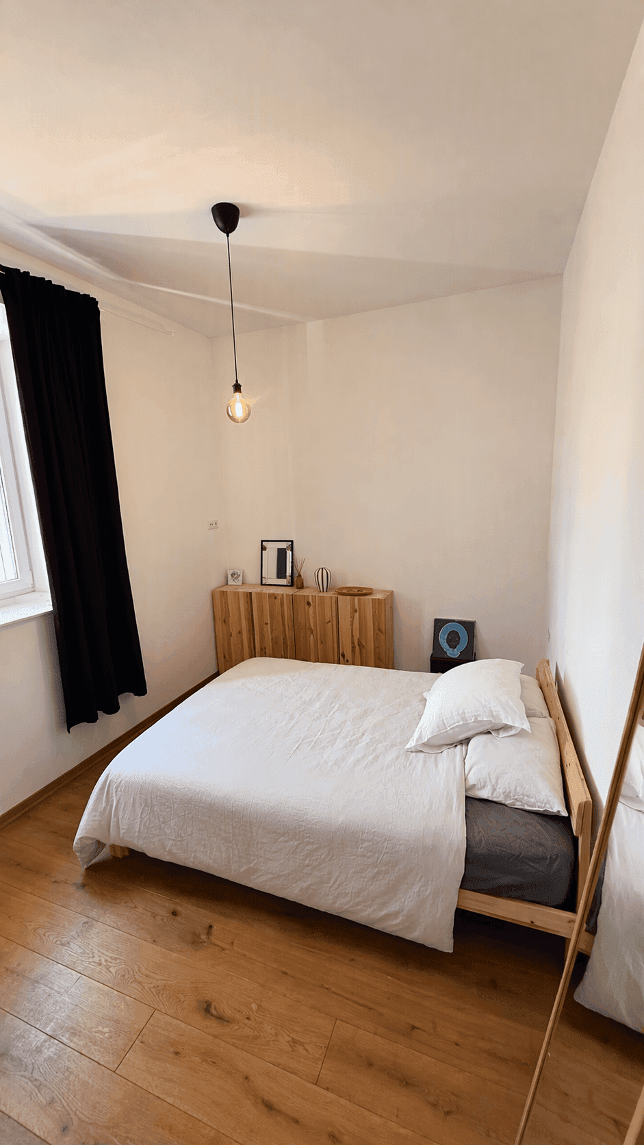 Helles Schlafzimmer mit Holzbett, Kommode und großem Spiegel.