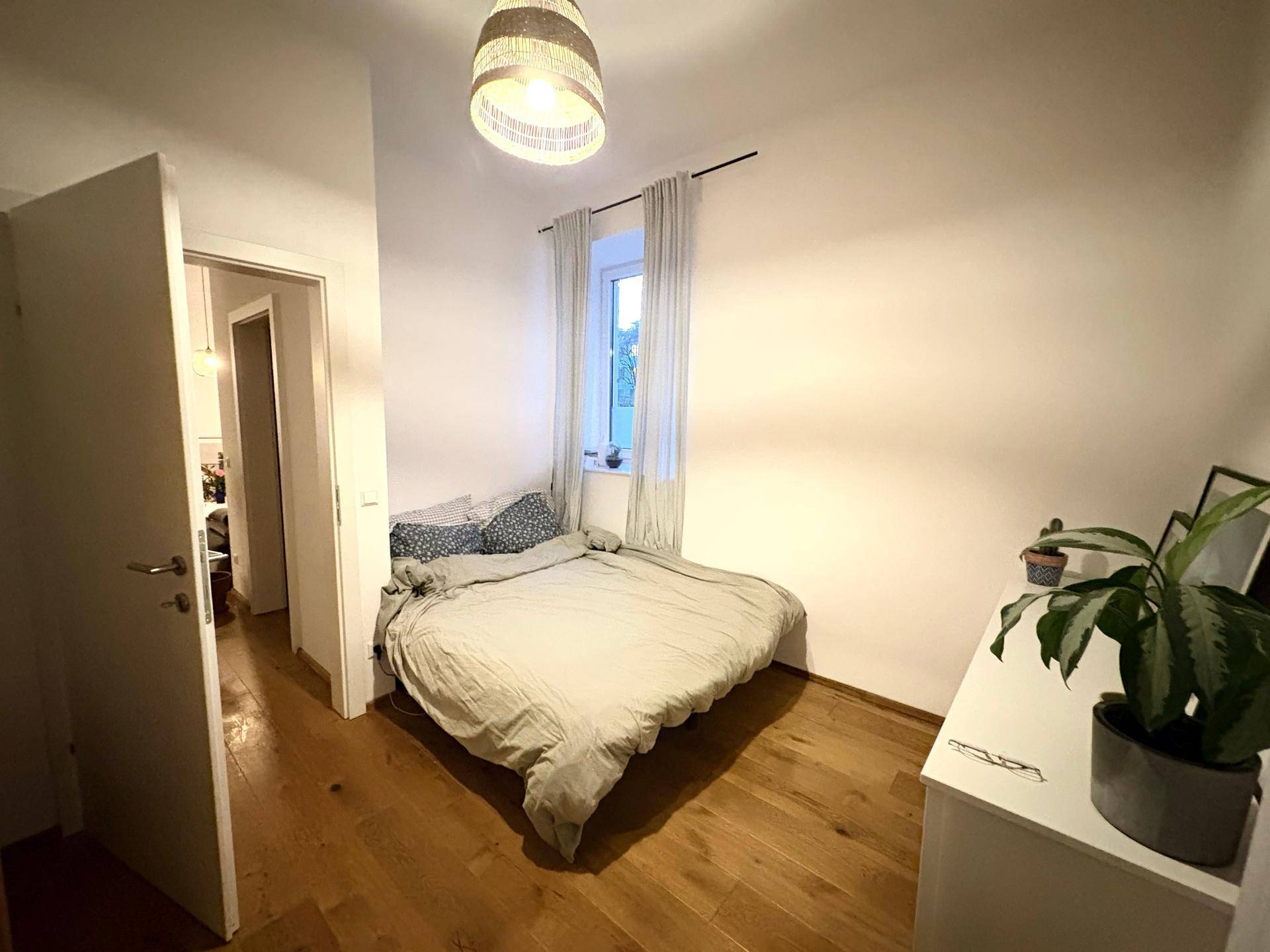 Helles Schlafzimmer mit Holzboden, Doppelbett und Fenster mit Vorhängen.
