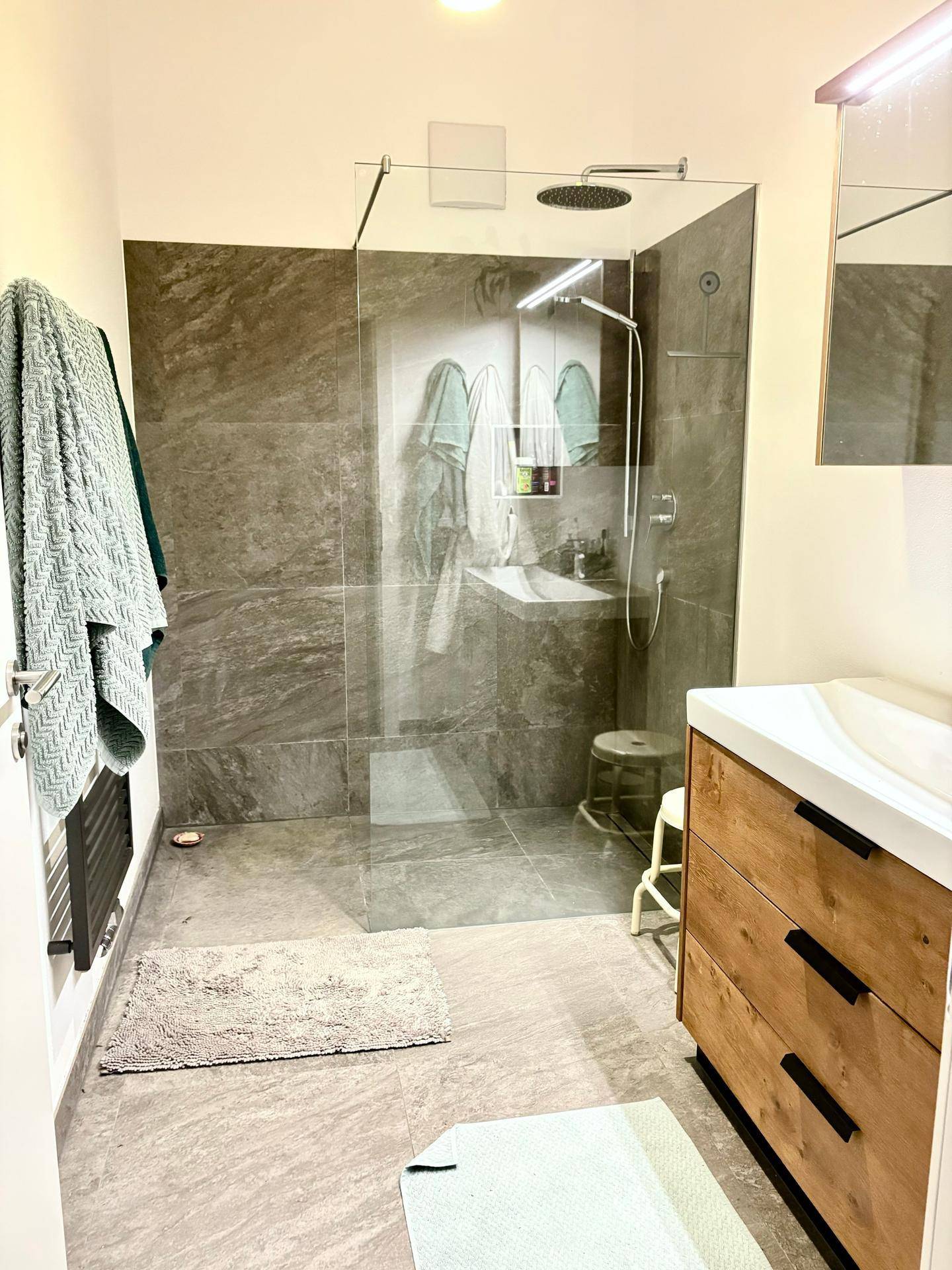 Geräumiges Badezimmer mit großer begehbarer Dusche, Holzwaschtisch und modernen Fliesen.