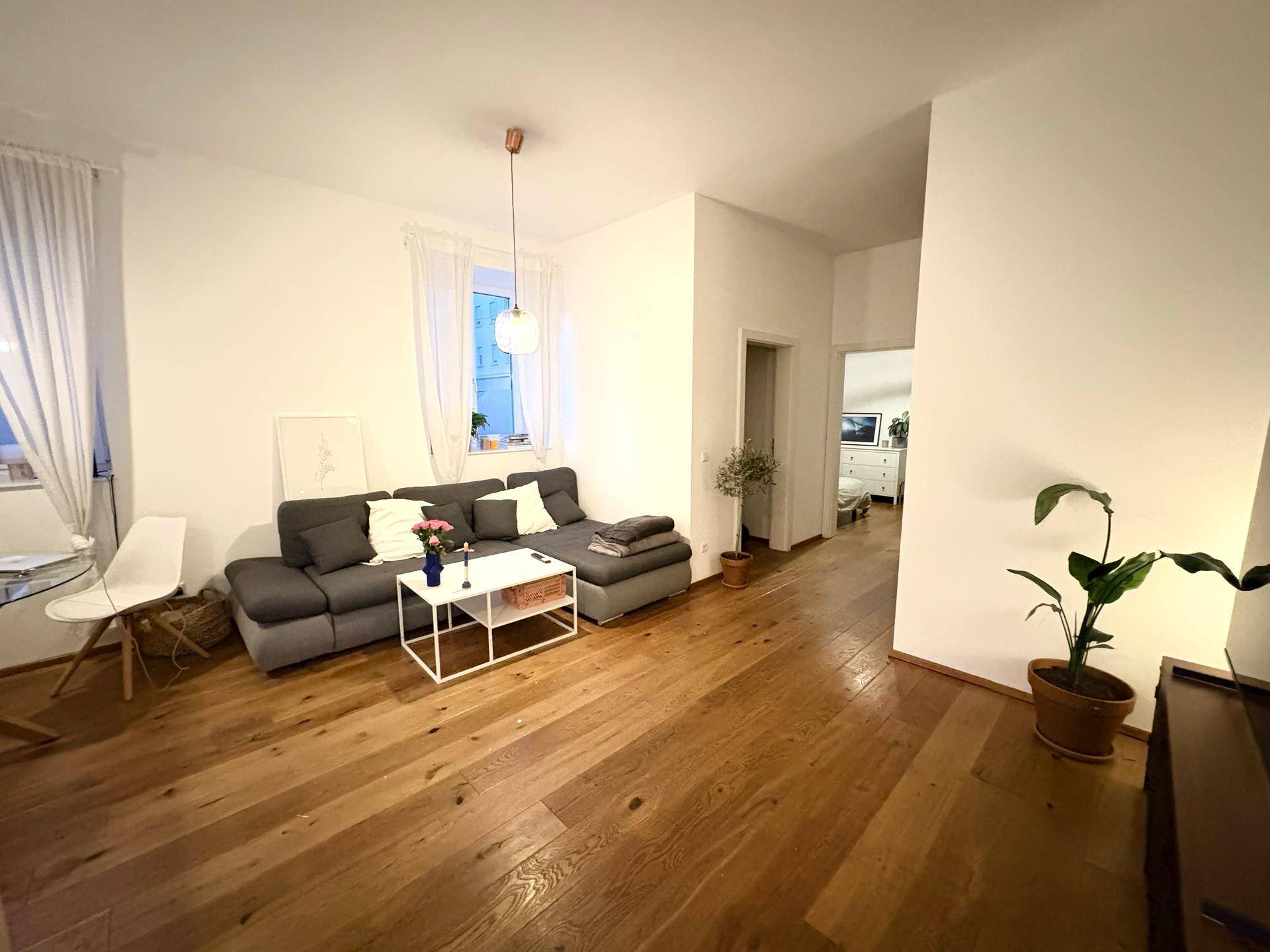 Gemütliches Wohnzimmer mit großem Ecksofa, Holzboden und Blick in den Flur.