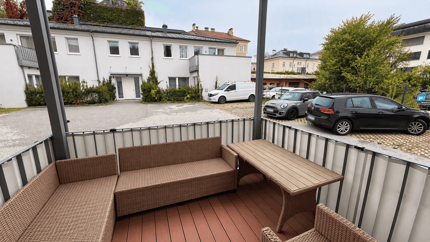 Große Terrasse mit Sitzgelegenheiten und Blick auf den Parkplatz und die Nachbargebäude.