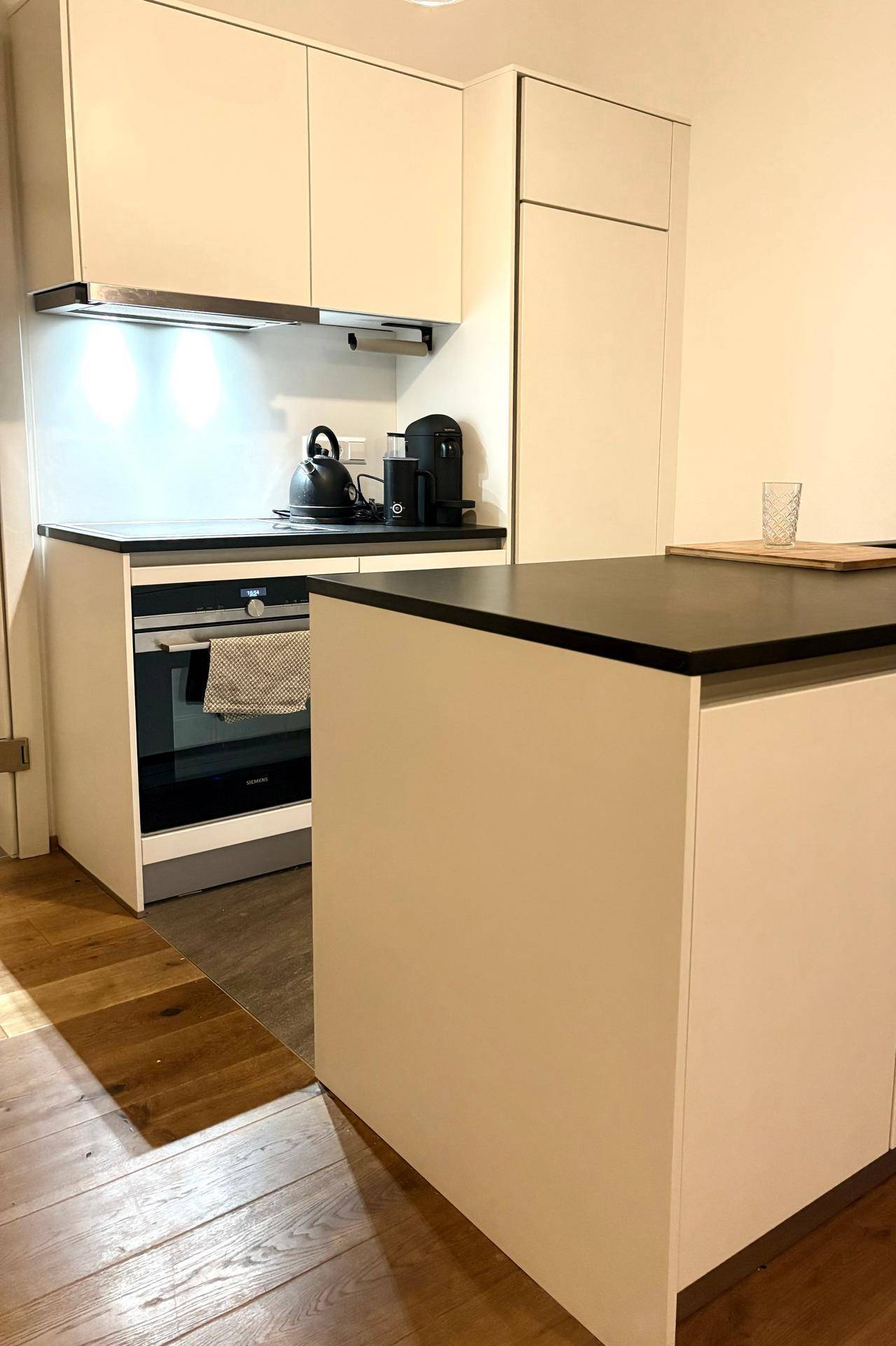 Moderne Einbauküche mit weißen Schränken, dunkler Arbeitsplatte und integriertem Backofen.
