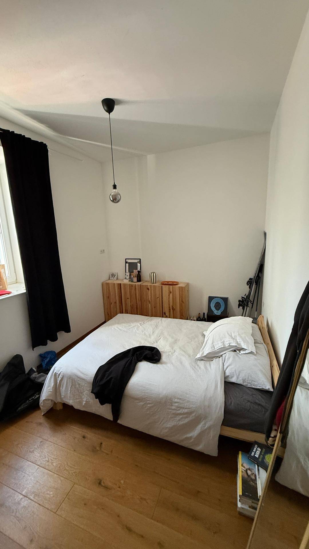 Schlafzimmer mit Holzboden, großem Bett und Fenster mit dunklem Vorhang.