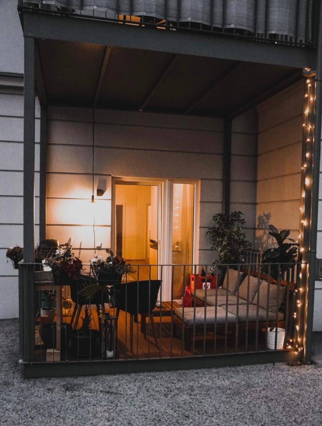 Gemütlicher Balkon mit Sitzgelegenheiten, Pflanzen und Lichterkette für abendliche Stunden.
