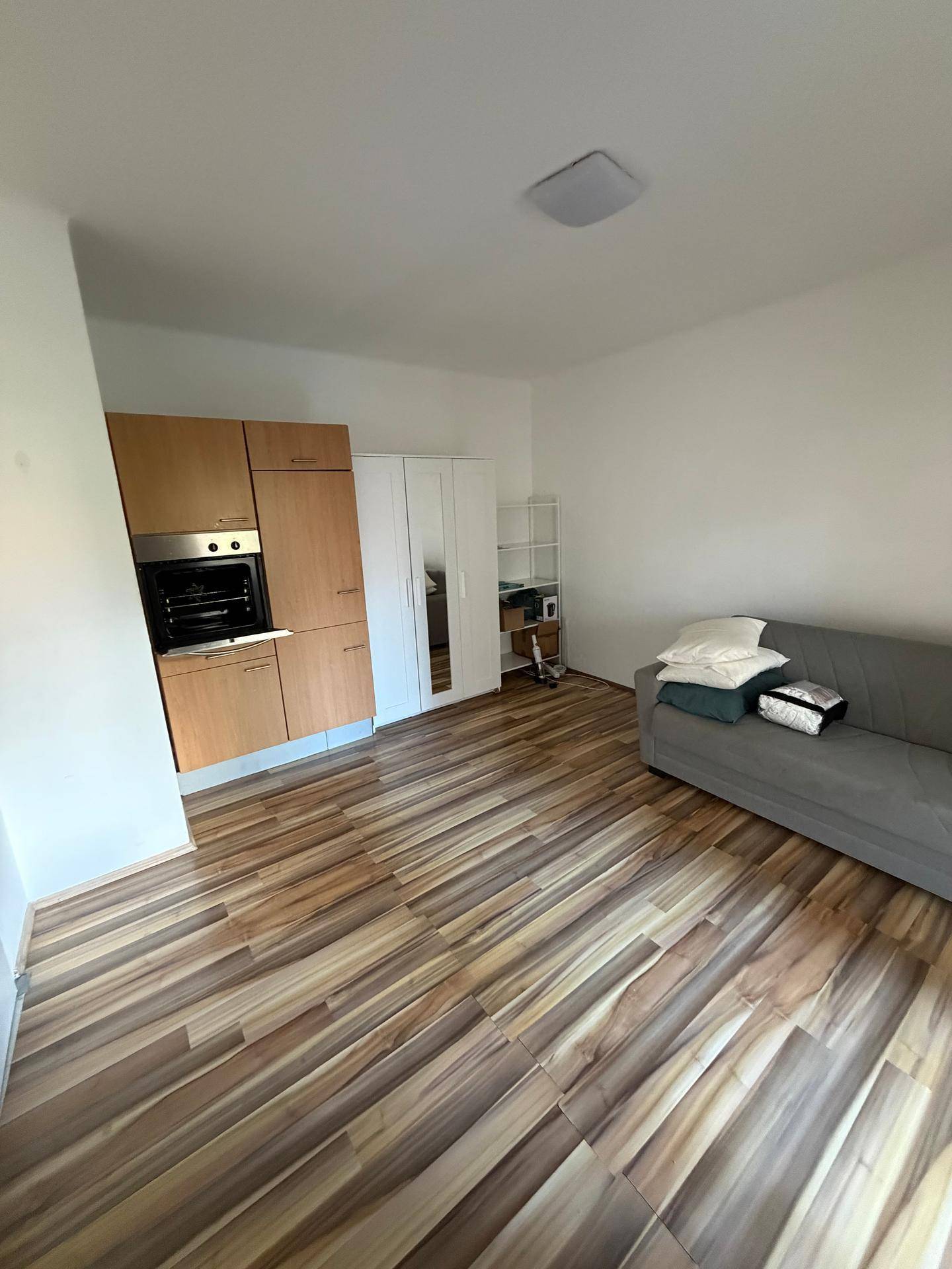 Wohnbereich mit Küchenzeile inklusive Backofen, Laminatboden und einem Kleiderschrank.
