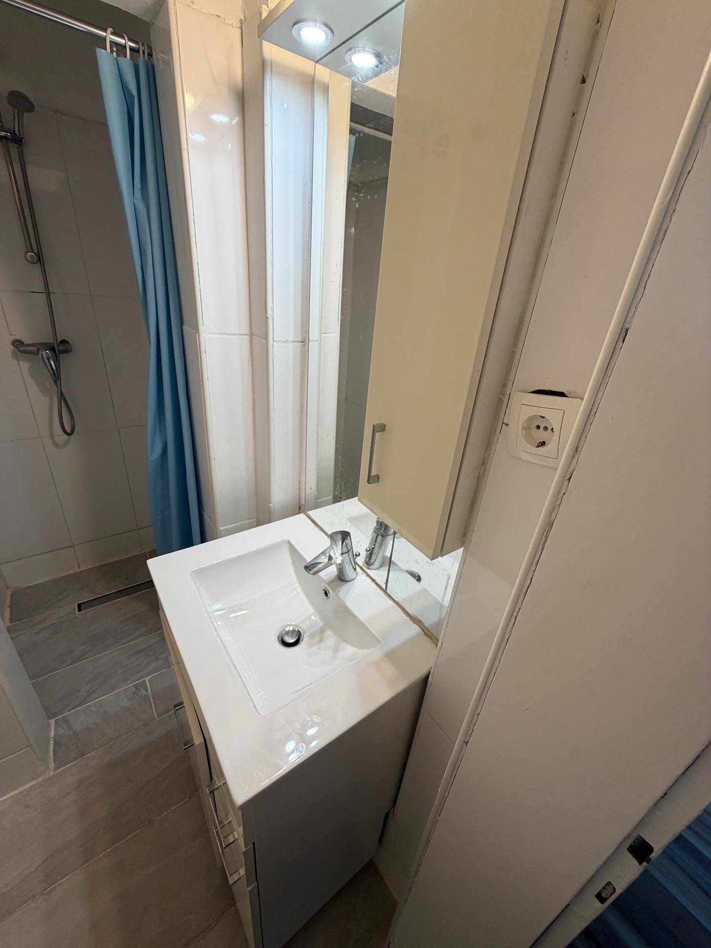 Waschbecken mit Spiegelschrank und Duschbereich, ausgestattet mit einem blauen Duschvorhang.